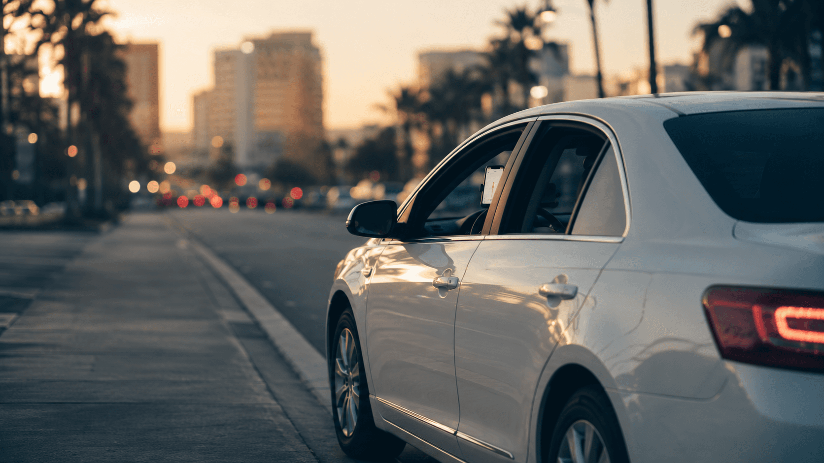 A white sedan at a city curb with a phone mounted on the dashboard for navigation